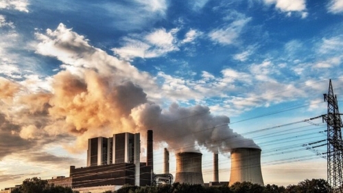 Emission plumes coming out of smokestacks, against a sunset sky
