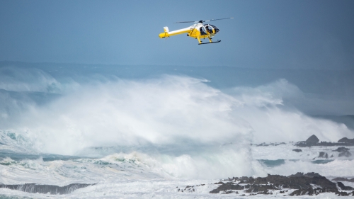 Waves crash as helicopter flies above