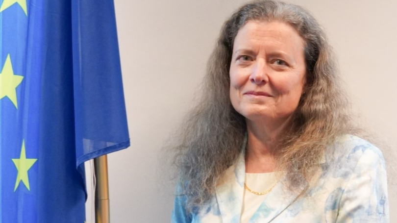 Anne Burrill stands in front of flag and smiles.