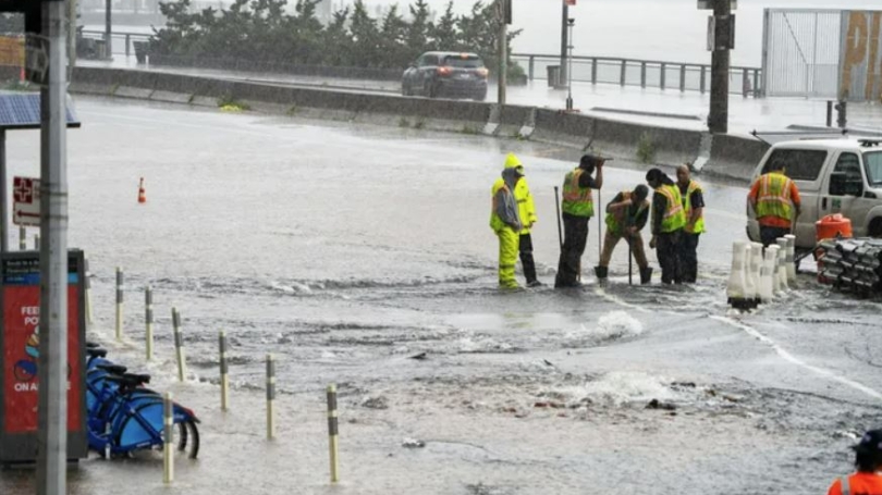 Workers try to clear culvert in street while up to ankles in water. 