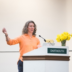 Professor Meredith Kelly Professor Meredith Kelly stands at a podium next to a vase with yellow flowers.